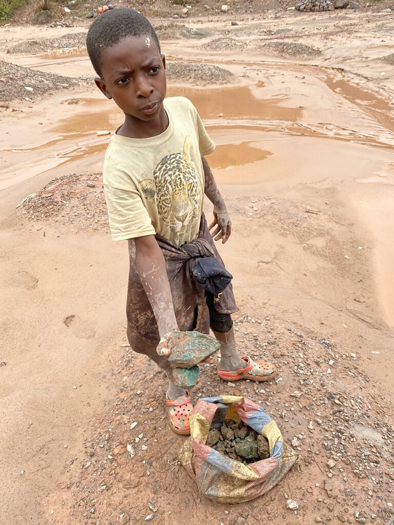 young African male holding piece of cobalt out of bag in wet, muddy mine quarry