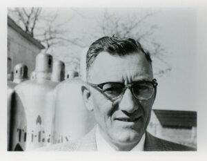 black and white old photo of senior adult male wearing a business suit with Tri-Gas containers behind him