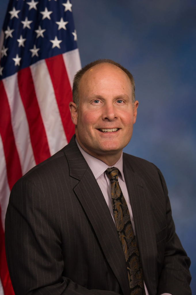 senior adult caucasian male in business attire sitting in front of American flag